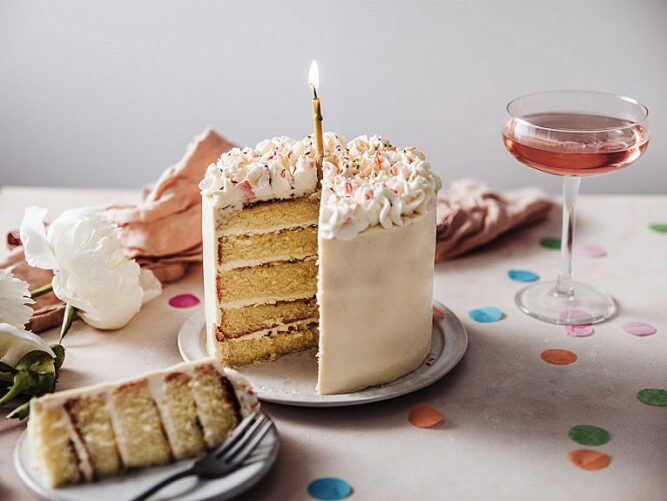 Pembe bir kokteylin yanındaki masada içinden bir dilim çıkarılmış doğum günü pastası.