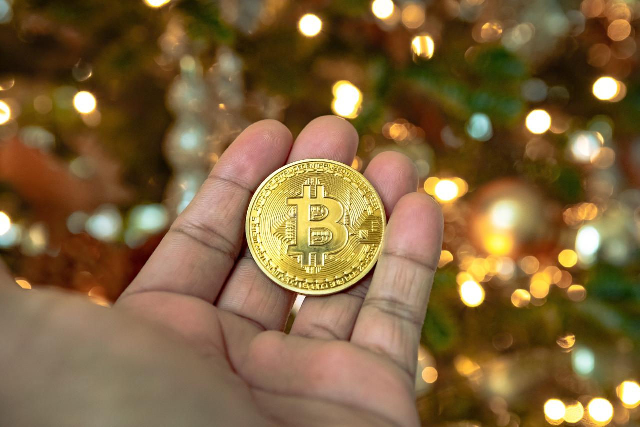 Bir kişi bir Noel ağacının önünde altın bir bitcoin parası tutuyor.